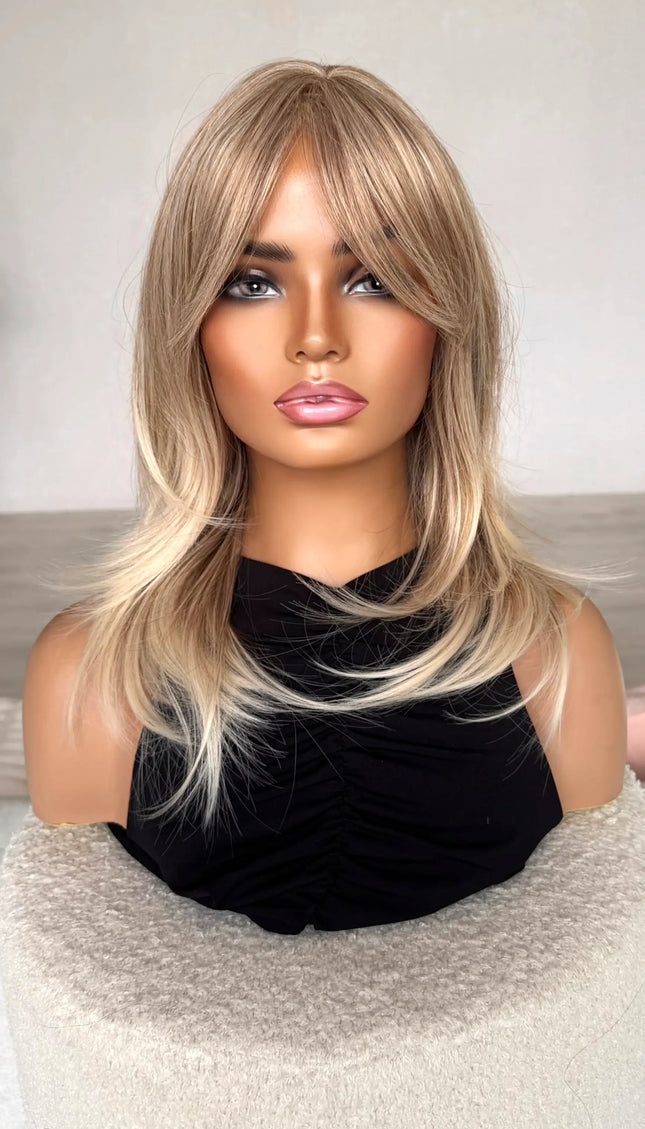 sandy blonde hair with curtain bangs/ fringe. front on view, lighter ends, middle part, heat safe hair. synthetic topper.