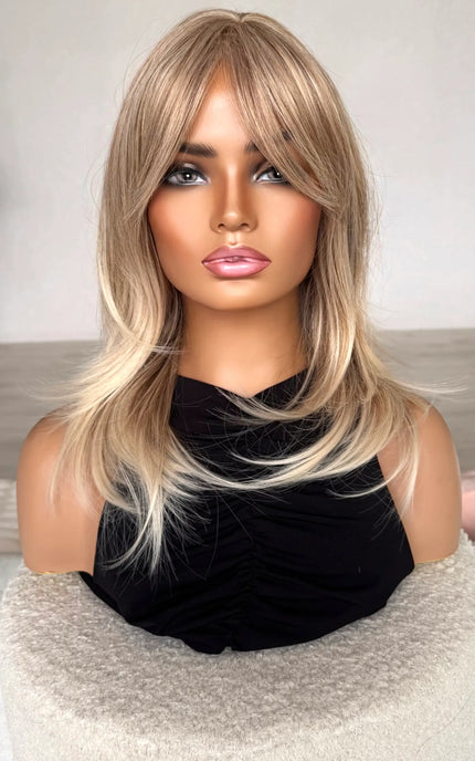 sandy blonde hair with curtain bangs/ fringe. front on view, lighter ends, middle part, heat safe hair. synthetic topper.