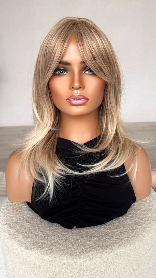 sandy blonde hair with curtain bangs/ fringe. front on view, lighter ends, middle part, heat safe hair. synthetic topper.