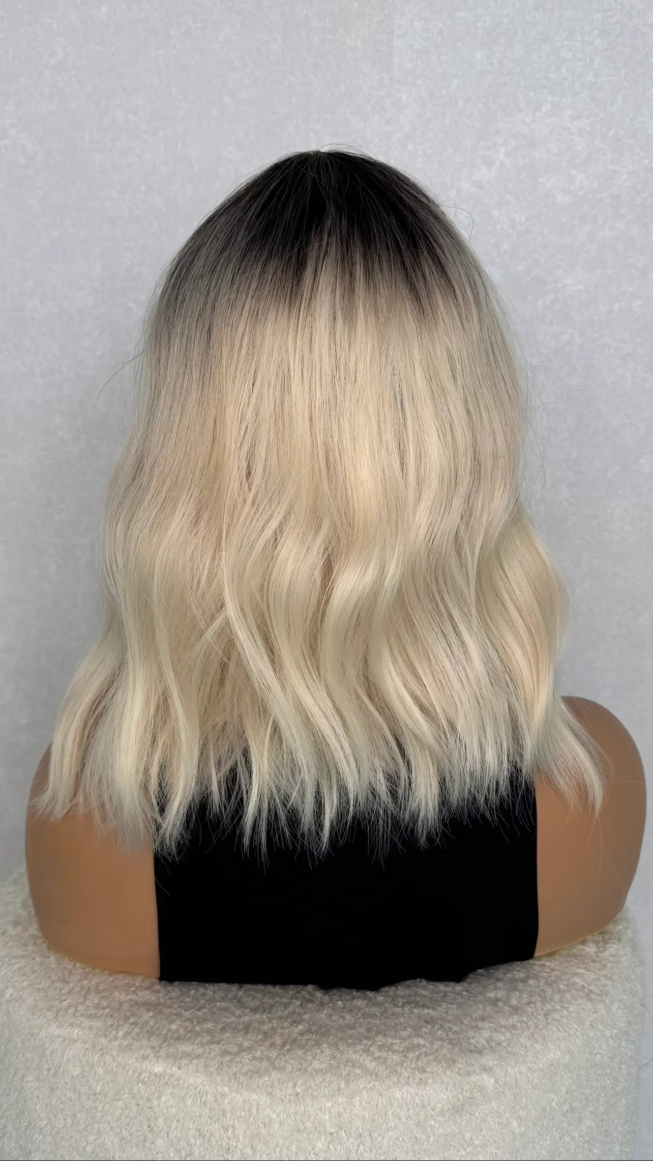 back view of synthetic fringe wig. blonde with dark root. wavy 