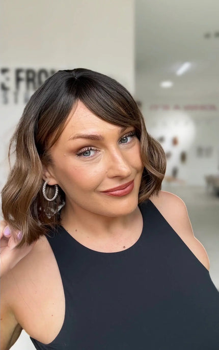 wavy hair wig with dark brunette roots to warm brown ends, midde part with long ispy fringe parted to the side.