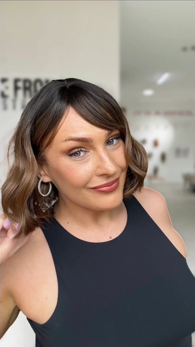 wavy hair wig with dark brunette roots to warm brown ends, midde part with long ispy fringe parted to the side.