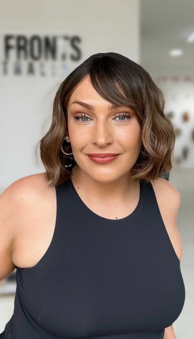 short wavy brunette bob with middle part, sitting just above shoulders, with fringe parted to the rigth hand side.