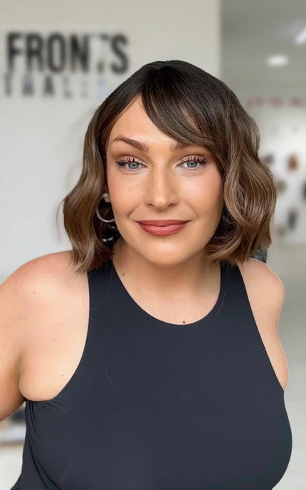 short wavy brunette bob with middle part, sitting just above shoulders, with fringe parted to the rigth hand side.