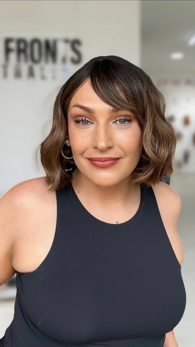 short wavy brunette bob with middle part, sitting just above shoulders, with fringe parted to the rigth hand side.