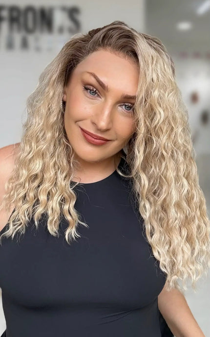 a side part on the curly honey blonde hair with soft brunette shadow root, lace front wig with natural looking hairline, designed for easy wear.