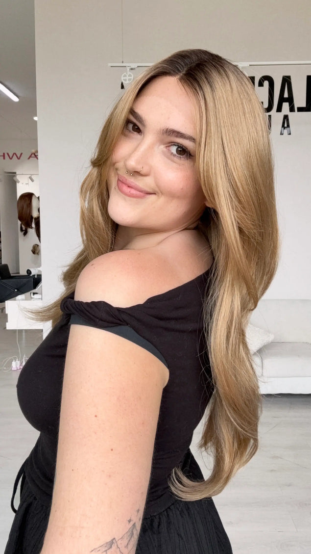 side view showing long length layered honey blonde hair, featuring a dark shadow root to dark honey blonde hair, this wig has a set middle part.