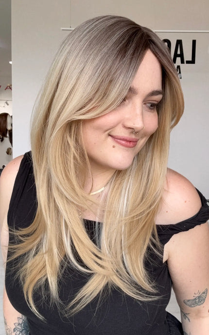 an easy to wear, layered blonde hair synthetic wig. for hairloss, alopecia, chemotherapy. a soft brunette root blending into a dimensional warm blonde range of colours.