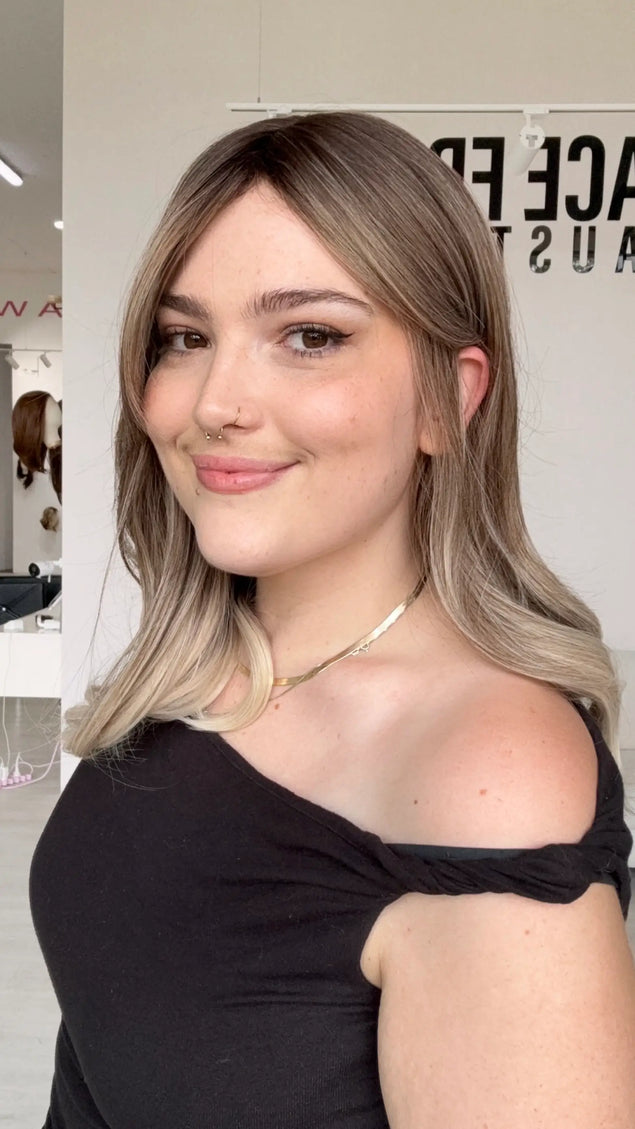 a side view showing ash blonde hair colour with a darker root, middle part and curtain bang fringe parted to the side, one ear tucked. 
