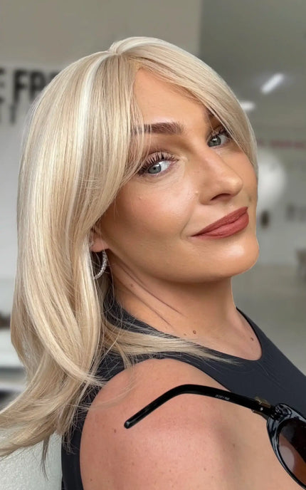 side view light creamy blonde hair with layers and long curtain bangs to frame the face.