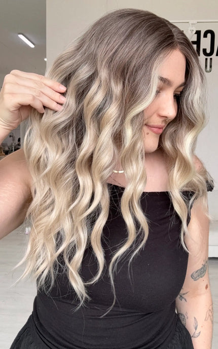 side view holding the long length beachy blonde wavy hair, middle part and wispy ends.