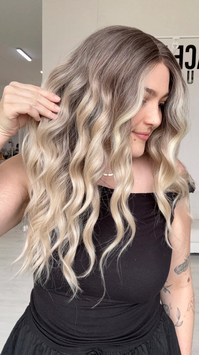 side view holding the long length beachy blonde wavy hair, middle part and wispy ends.
