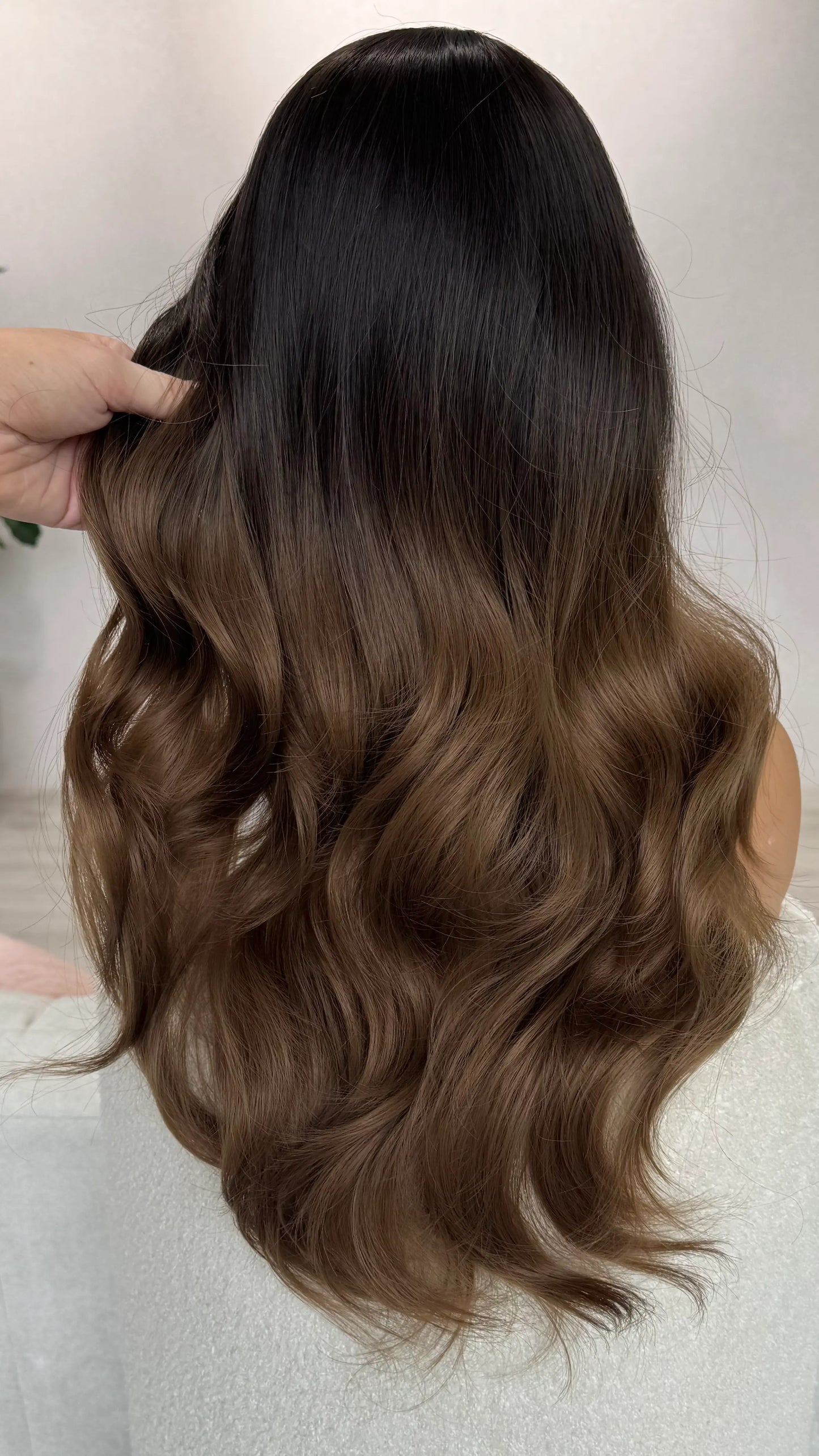 back view of holding the wavy hair. showing soft blend of dark to ligh brown hair. heat safe hair.