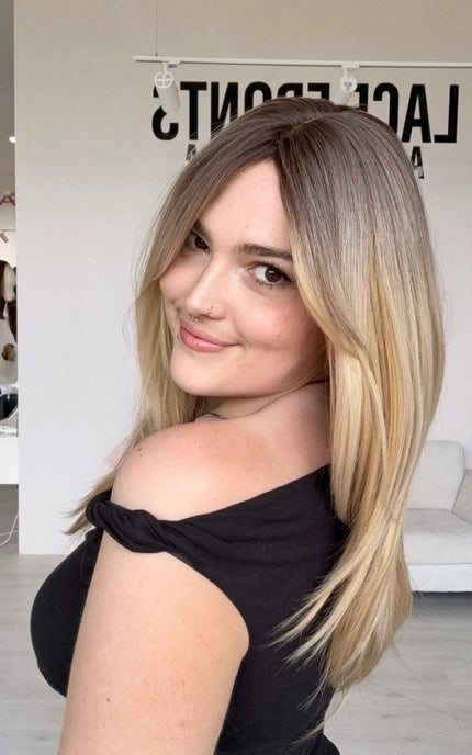 a soft brunette root blending into a creamy warm blonde, layered hairstyle. long curtain bang fringe parted to the side, heat safe hair and a glueless cap with adjsutable straps for easy everyday wear.