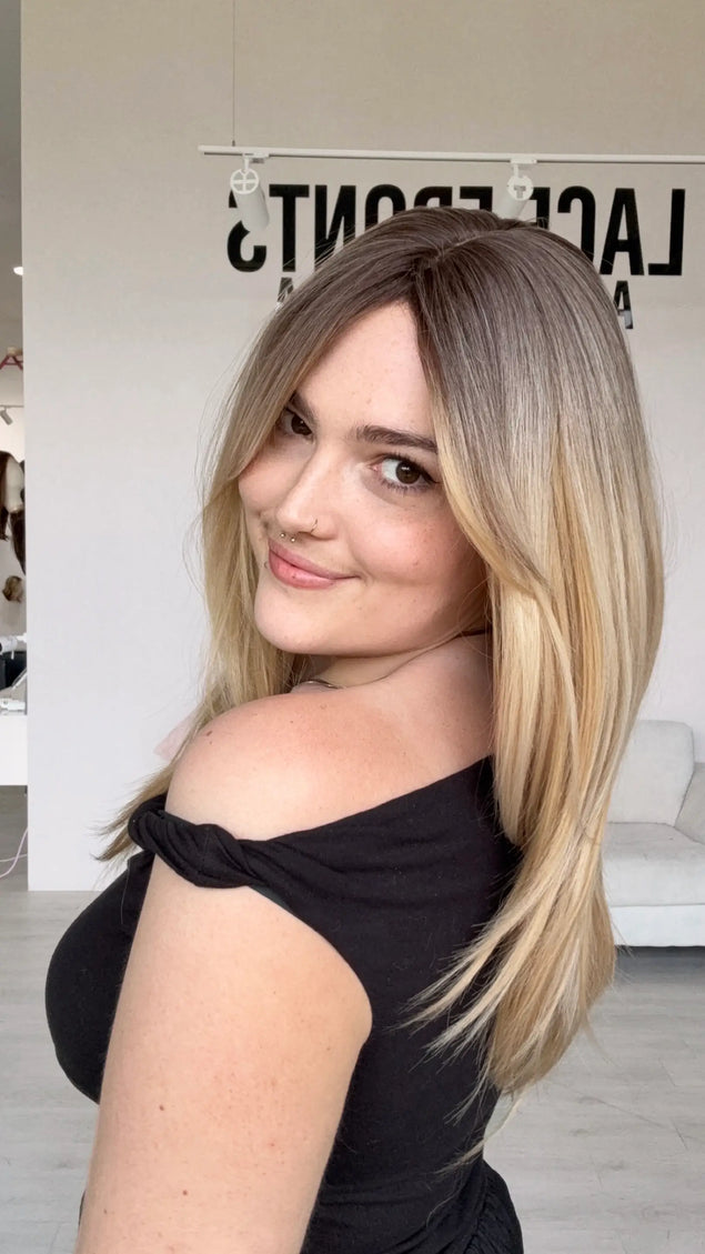 a soft brunette root blending into a creamy warm blonde, layered hairstyle. long curtain bang fringe parted to the side, heat safe hair and a glueless cap with adjsutable straps for easy everyday wear.