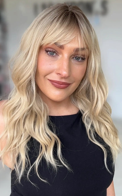 a women wearing a soft warm blonde wavy hair natural looking wig with a aoft shadow root, medium chest length wavy blonde hair.