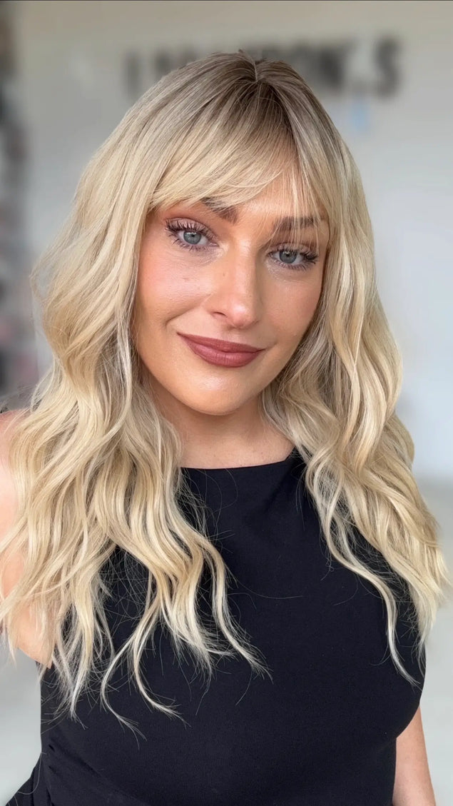 a women wearing a soft warm blonde wavy hair natural looking wig with a aoft shadow root, medium chest length wavy blonde hair.